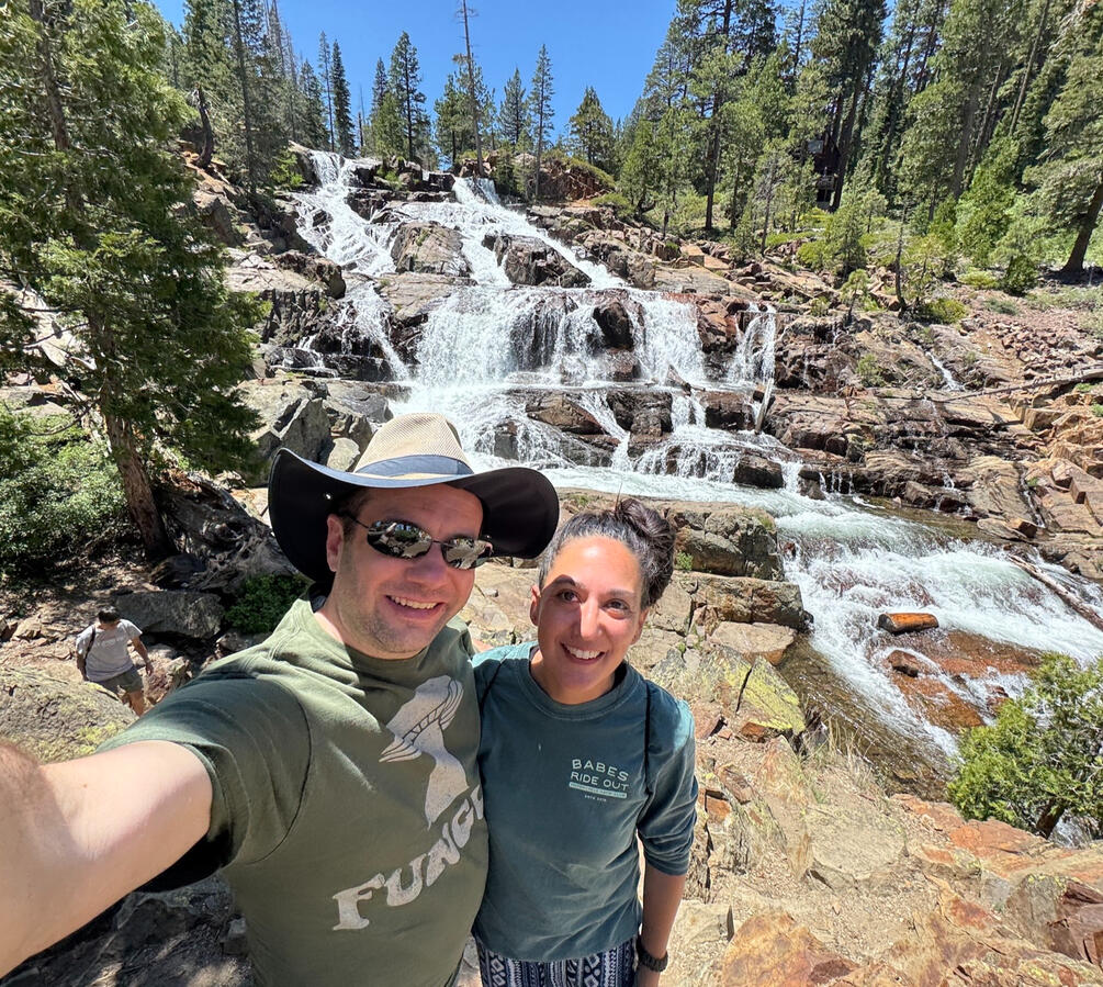 Michael and Michelle selfie in front of a series of small waterfalls in the background, surrounded by trees.